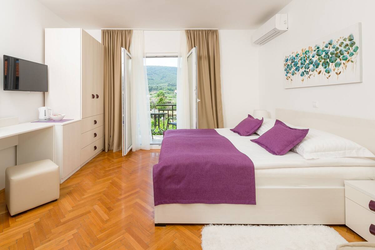 A bedroom with a bed, a desk, a chair, and a view of a balcony.