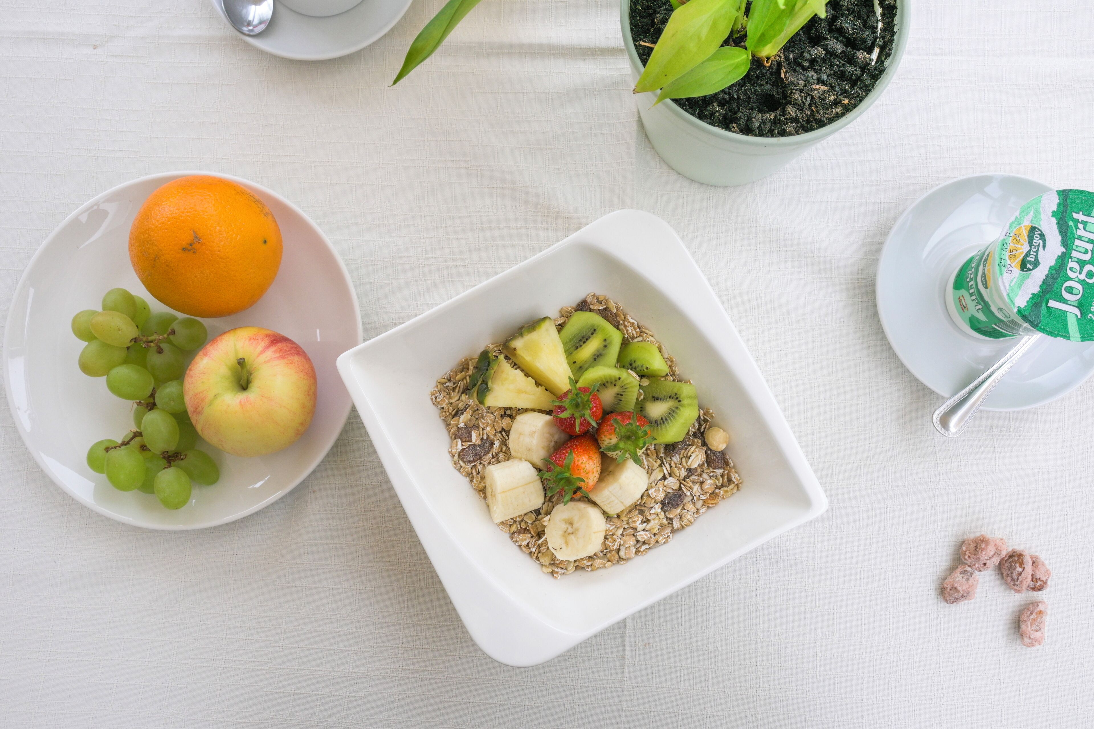 Una mesa blanca con dos platos blancos, uno con frutas y el otro con un cuenco de cereal.