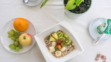 Una mesa blanca con dos platos blancos, uno con frutas y el otro con un cuenco de cereal.