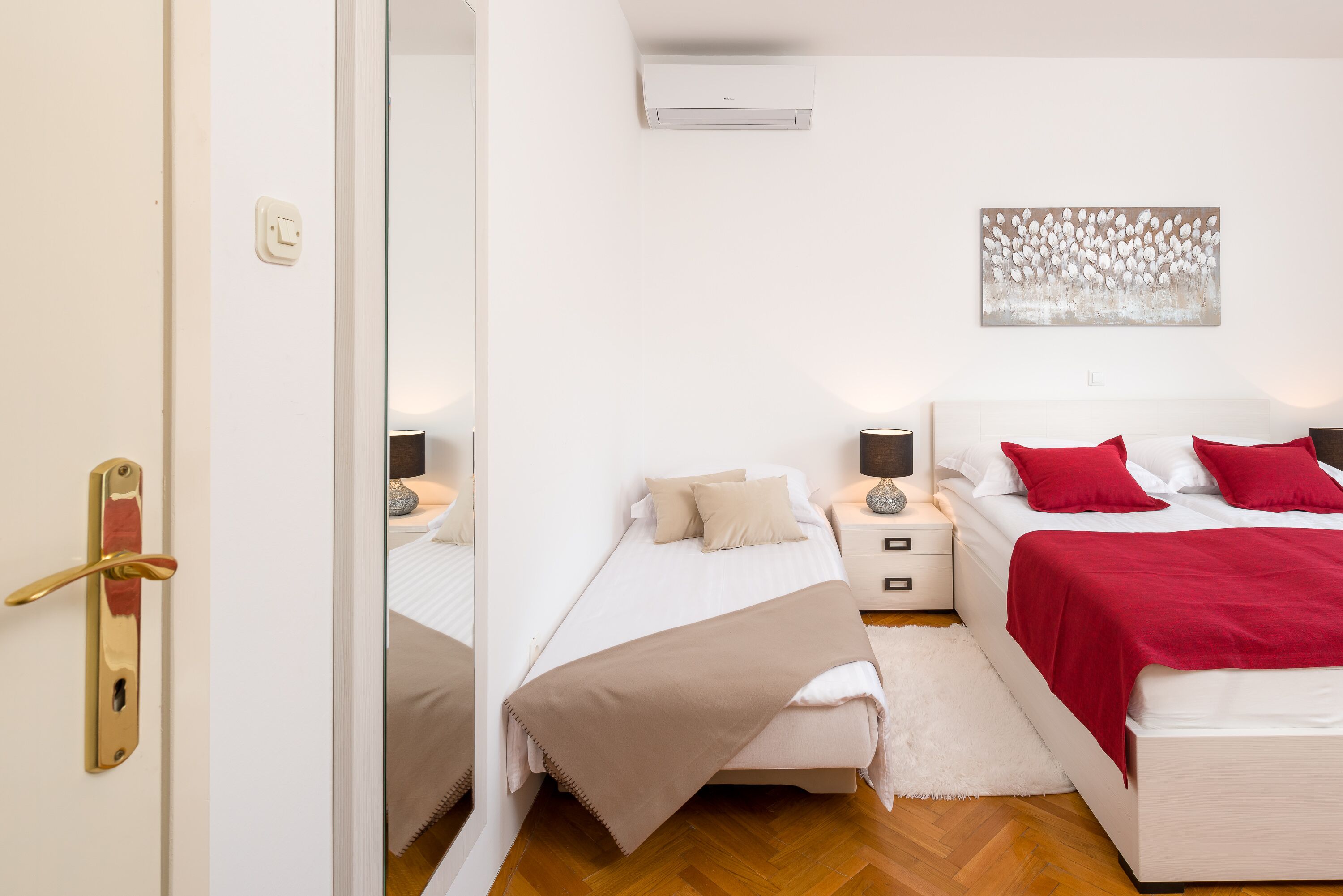 Habitación de hotel con dos camas, una pared blanca, un aire acondicionado y un cuadro.