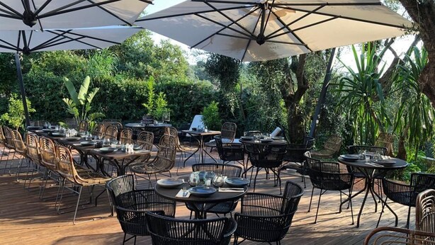 An outdoor dining area with multiple tables and chairs, surrounded by umbrellas and greenery. - Hôtel Avocado (Saint-Jeannet)