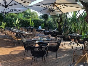 Un área de comedor al aire libre con varias mesas y sillas, rodeada de sombrillas y vegetación.