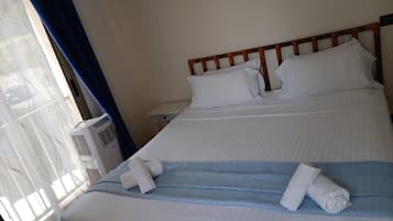 A hotel room with a bed, a nightstand, a window with curtains, and an air conditioning unit.