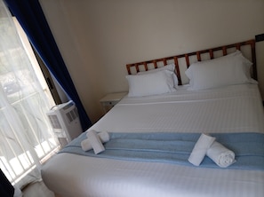 Une chambre d’hôtel comprenant un lit, une table de chevet, une fenêtre avec des rideaux et un appareil de climatisation.