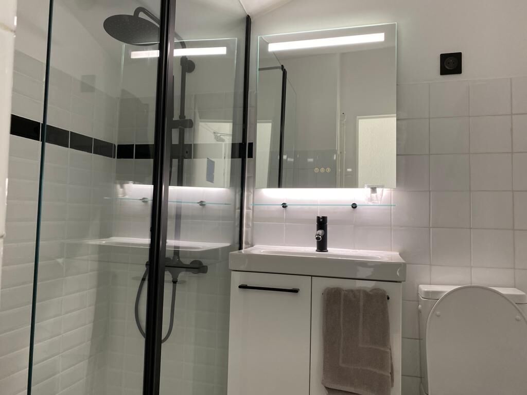 Et moderne badeværelse med en brusekabine i glas, en hvid vask med spejl over, og et toilet.