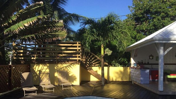 A pool area with a wooden deck, lounge chairs, and a covered seating area. - ti case gwada bungalow rentals "ti dauphin" (Sainte-Anne)