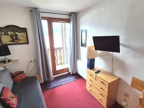 Une chambre d’hôtel comprenant un lit, une commode en bois, un téléviseur et une porte donnant sur un balcon.