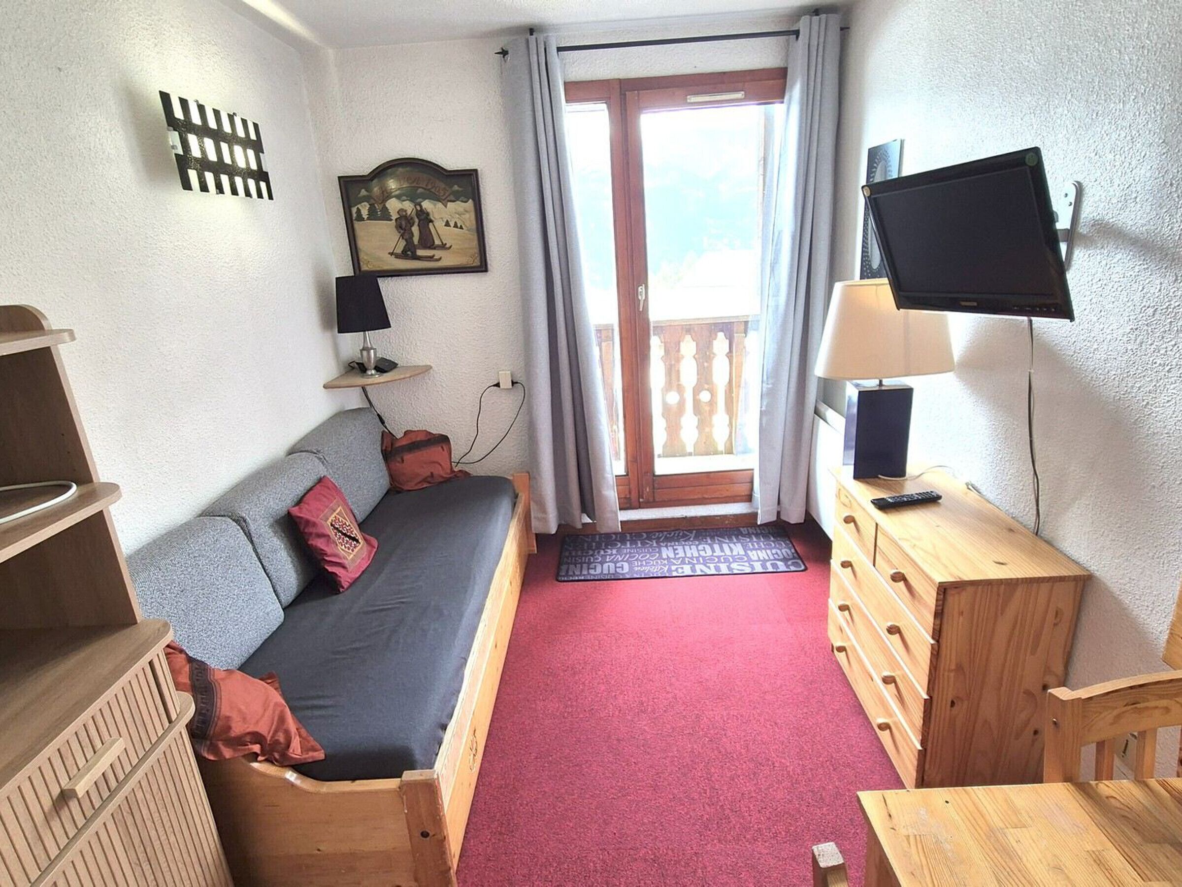 A small, cozy room with a sofa, a TV, a wooden dresser, and a window with a view.