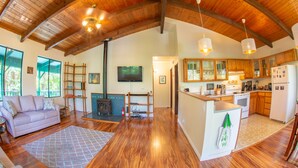 A spacious living area with a wooden ceiling, a fireplace, a sofa, and a kitchen with wooden cabinets and appliances. - 6 mins from Nat'l Park! Enjoy the sound of rain & birds in a peaceful retreat. (Volcano)