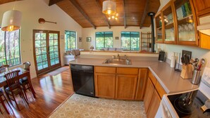 A spacious kitchen with wooden cabinets, a dishwasher, and a large island. There are windows with a view of greenery outside. - 6 mins from Nat'l Park! Enjoy the sound of rain & birds in a peaceful retreat. (Volcano)