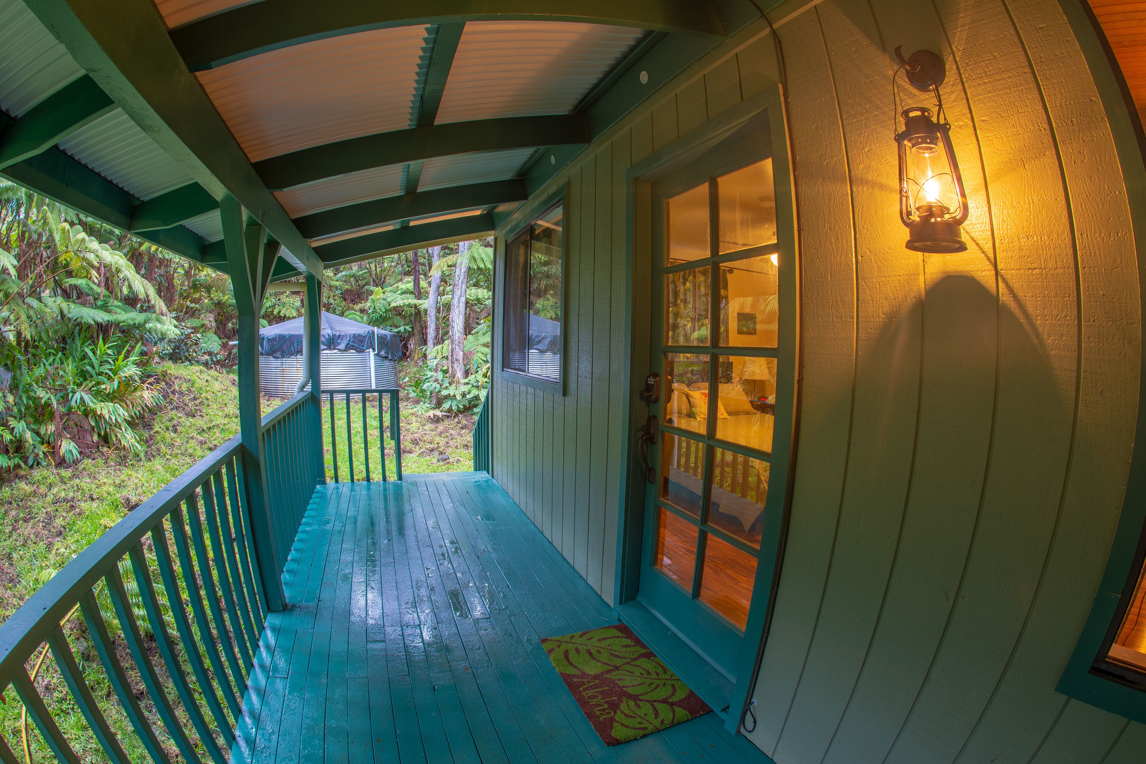 A porch with a wooden railing, a door with glass panels, and a lantern on the wall.