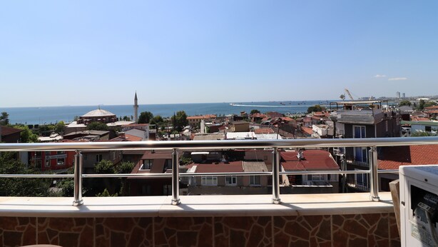 A balcony with a view of a coastal town, including buildings and a mosque.