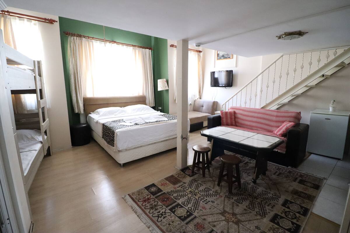 A room with a bunk bed, a desk with a chair, a sofa, a TV, and a staircase.