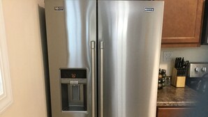 Un réfrigérateur en acier inoxydable doté d’un distributeur d’eau, d’un autocollant indiquant une garantie de 10 ans et du logo Maytag.