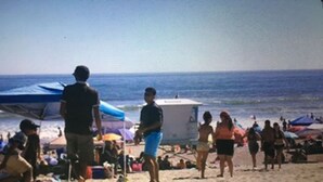 Une scène de plage avec des personnes qui se promènent et qui sont debout, une tour de surveillance des sauveteurs et des parasols.