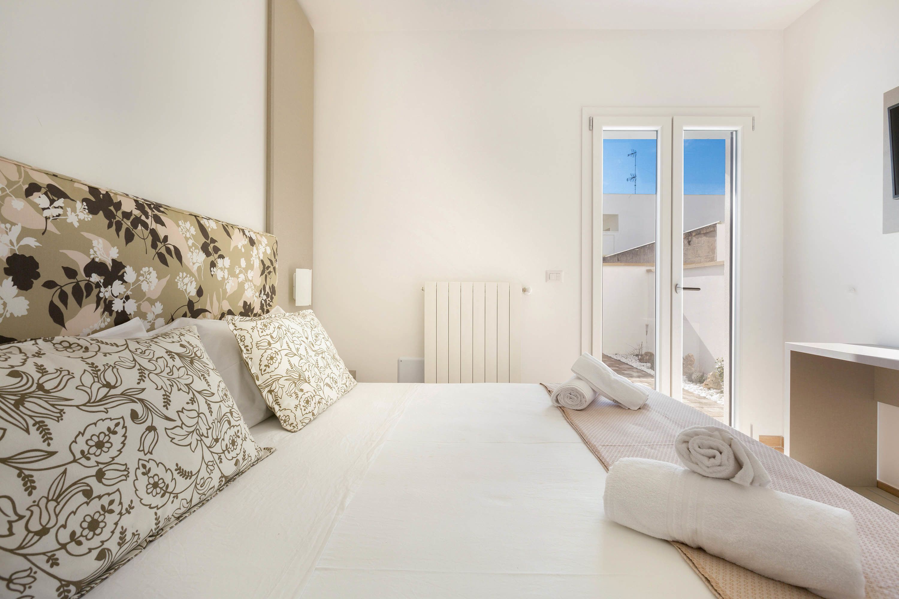 Un dormitorio con cama, almohadas, una toalla enrollada, un radiador y vistas al exterior.