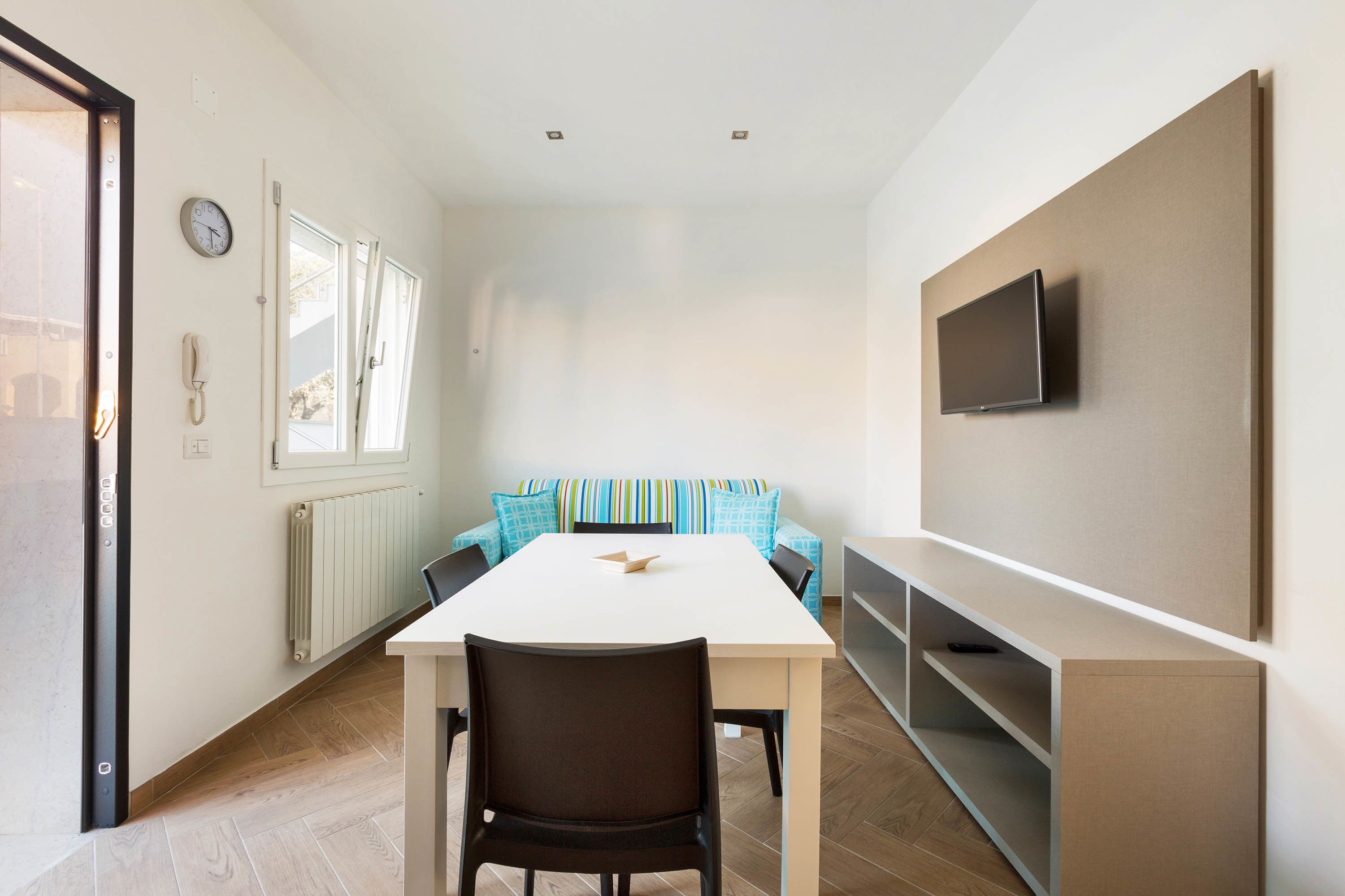 Una sala moderna con un sofá blanco, una mesa de comedor y un televisor montado en la pared.
