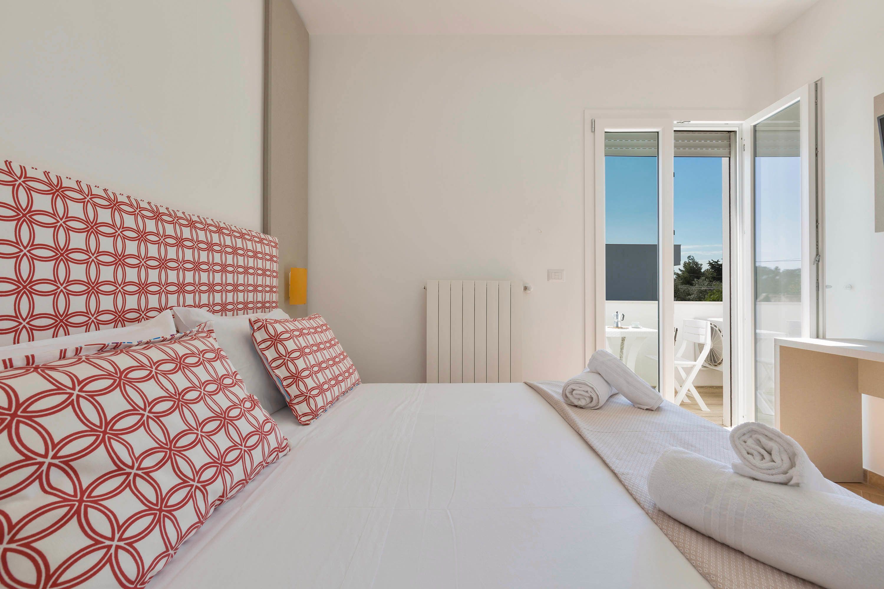 A hotel room with a bed, pillows, a radiator, a window, and a balcony.
