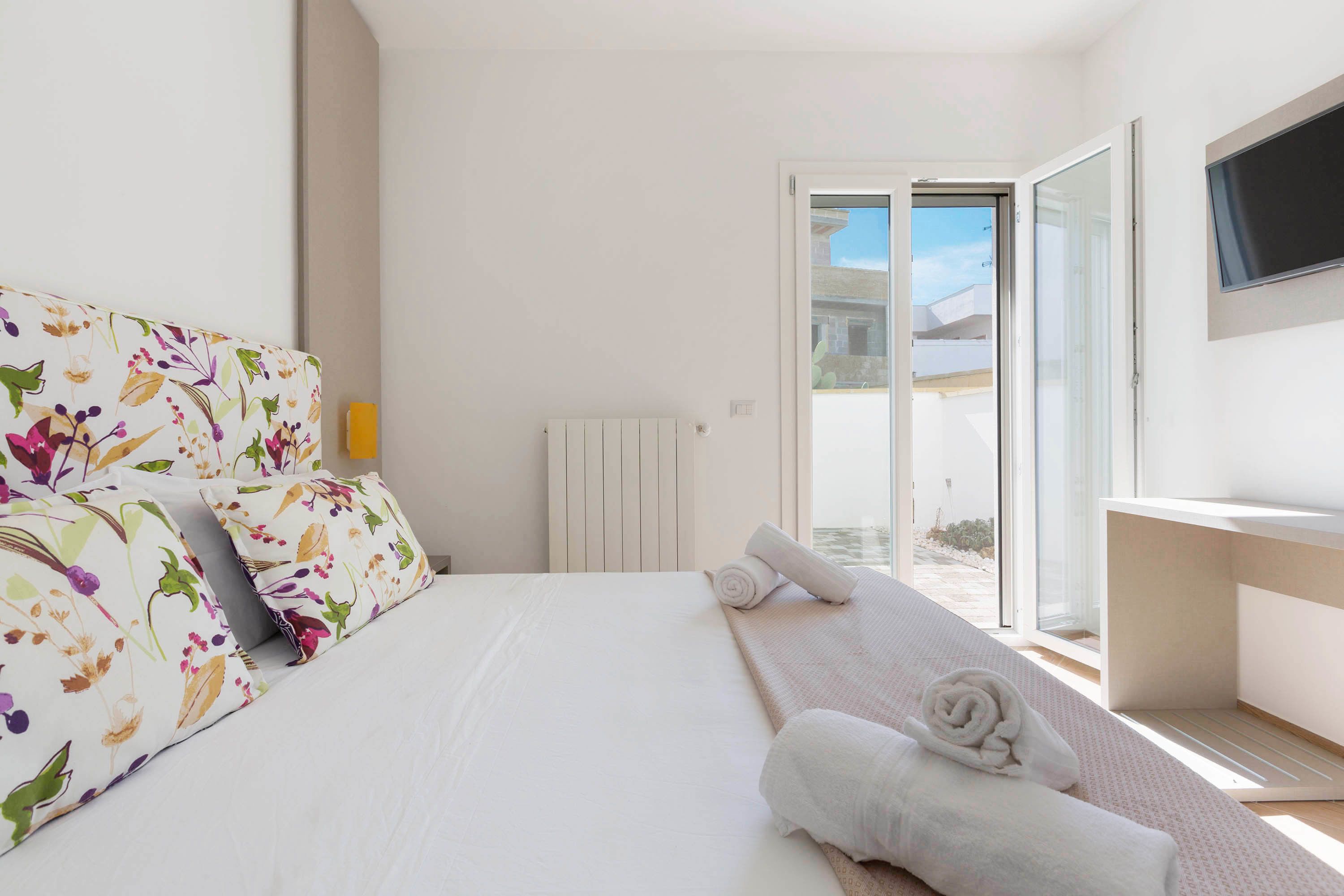 A hotel room with a bed, a TV, a window, and a view of the outside.