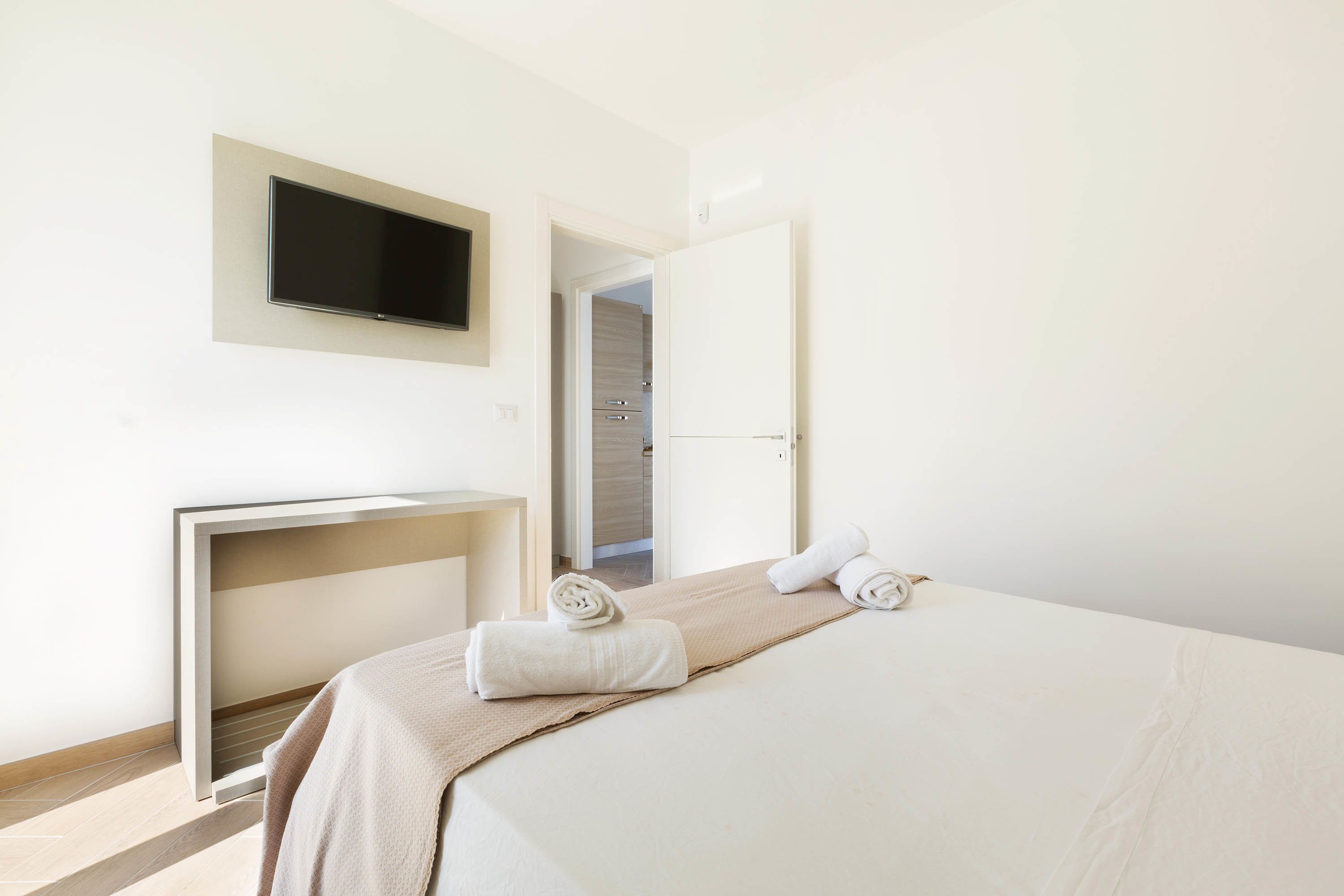A hotel room with a bed, a flat-screen TV mounted on the wall, a desk, and a walk-in closet.