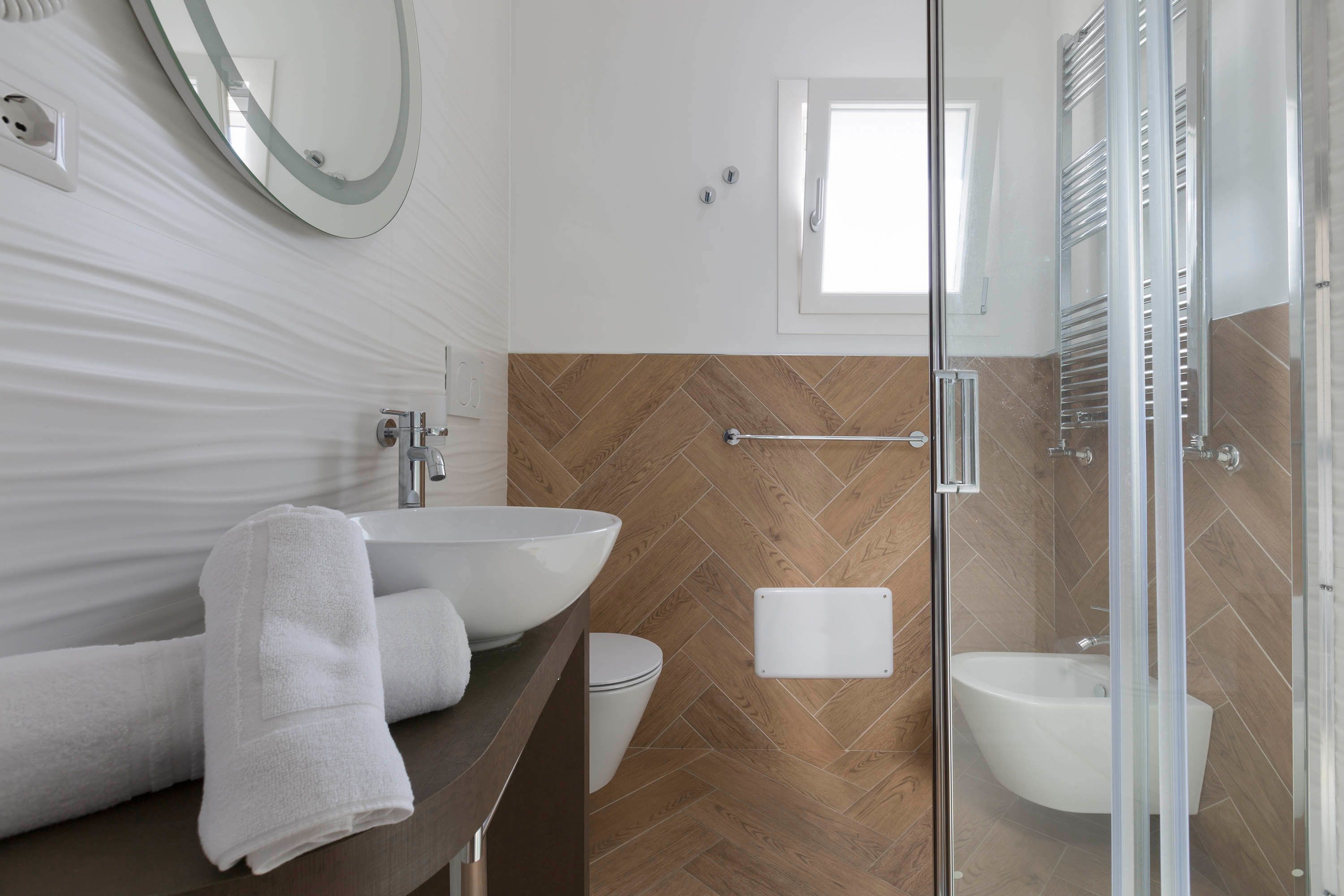 A modern bathroom with a large sink, a glass shower enclosure, and a herringbone-patterned wall.