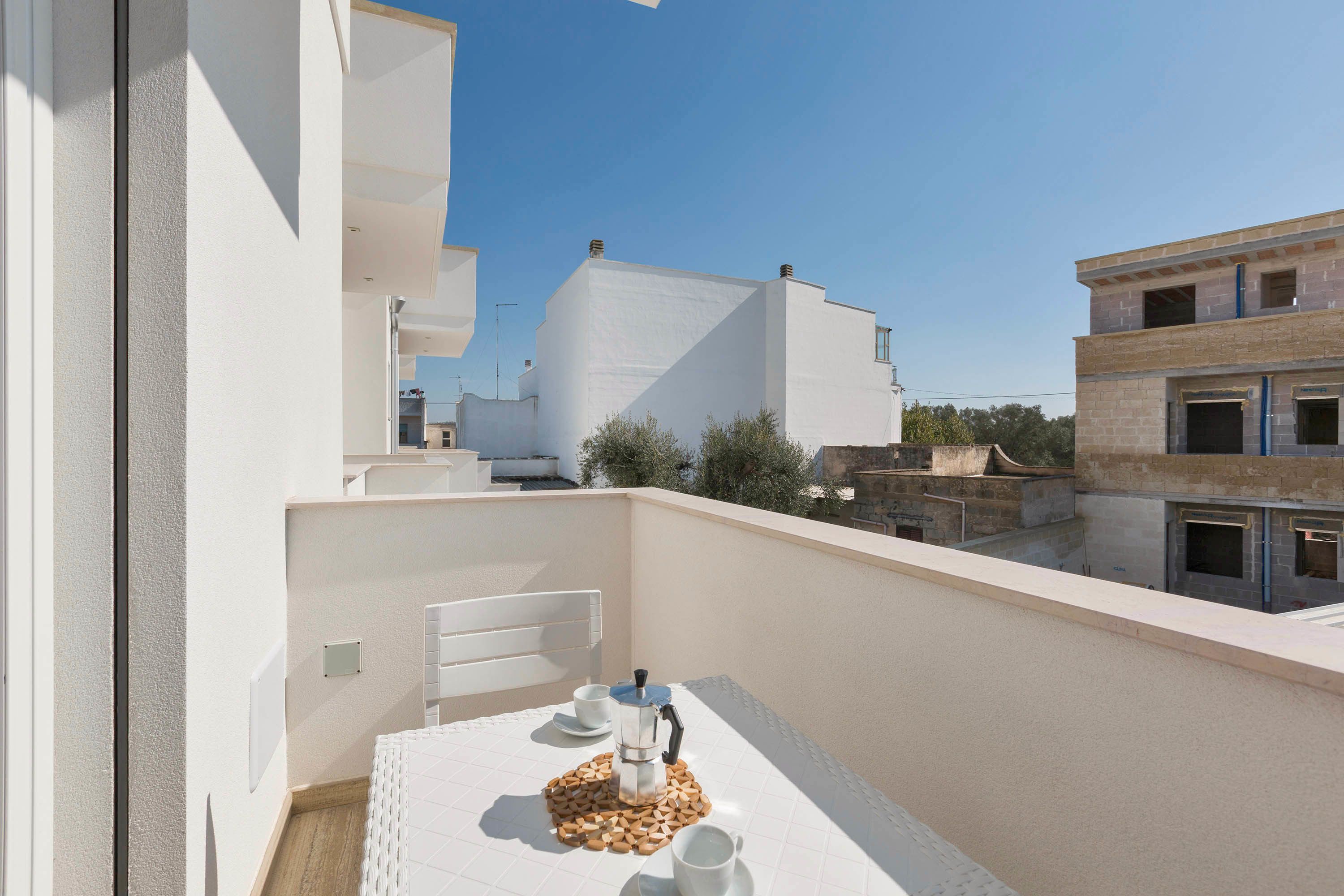 A balcony with a table set for two, a coffee maker, and a cup.