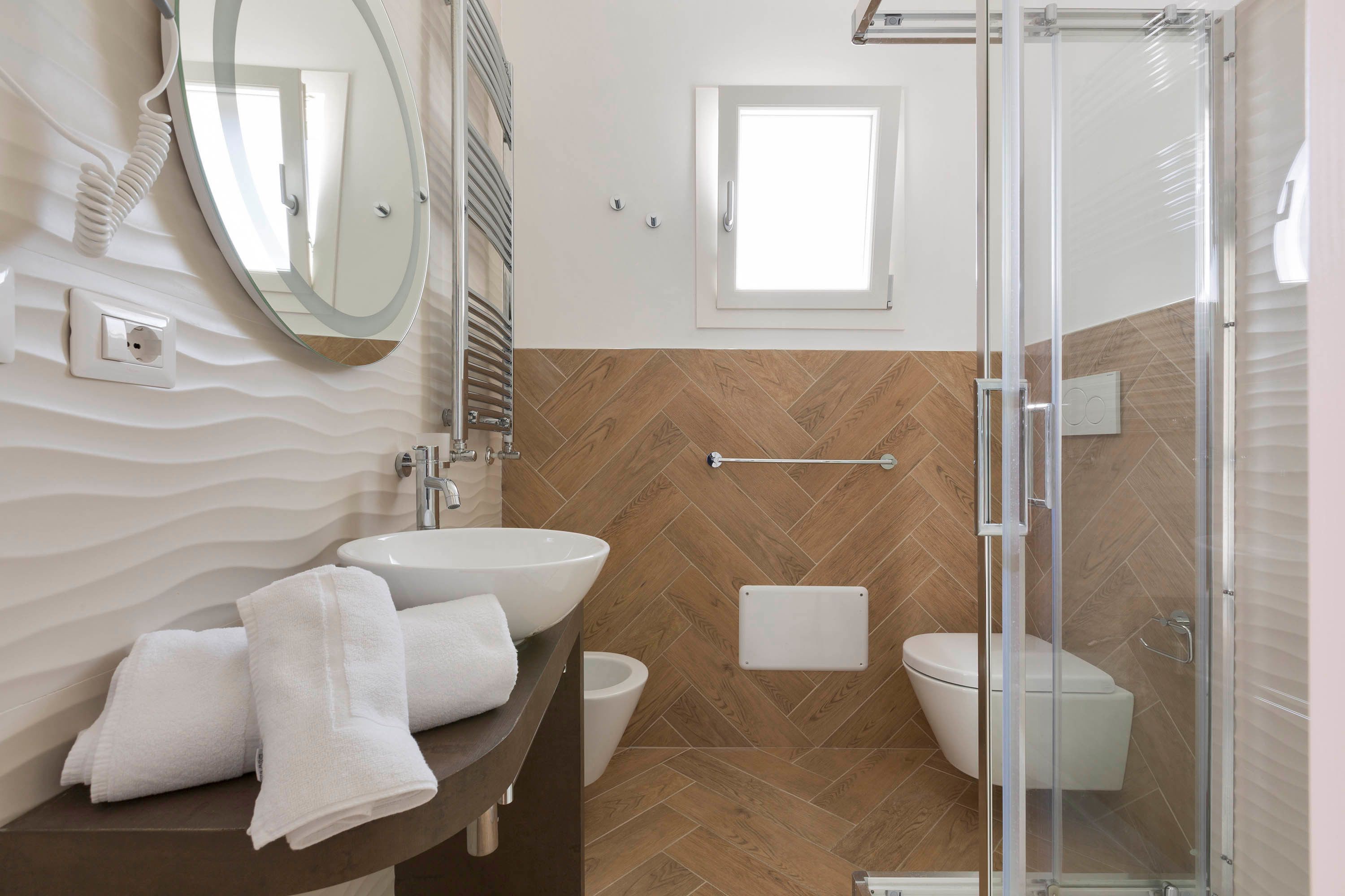 A bathroom with a round mirror, a sink, a toilet, and a shower enclosure.