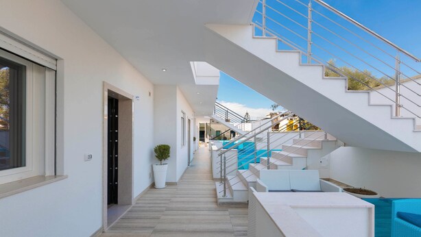 A modern interior with a staircase leading to an upper level, a seating area with blue cushions, and a potted plant. - Absolute Suite Apartments (Porto Cesareo)