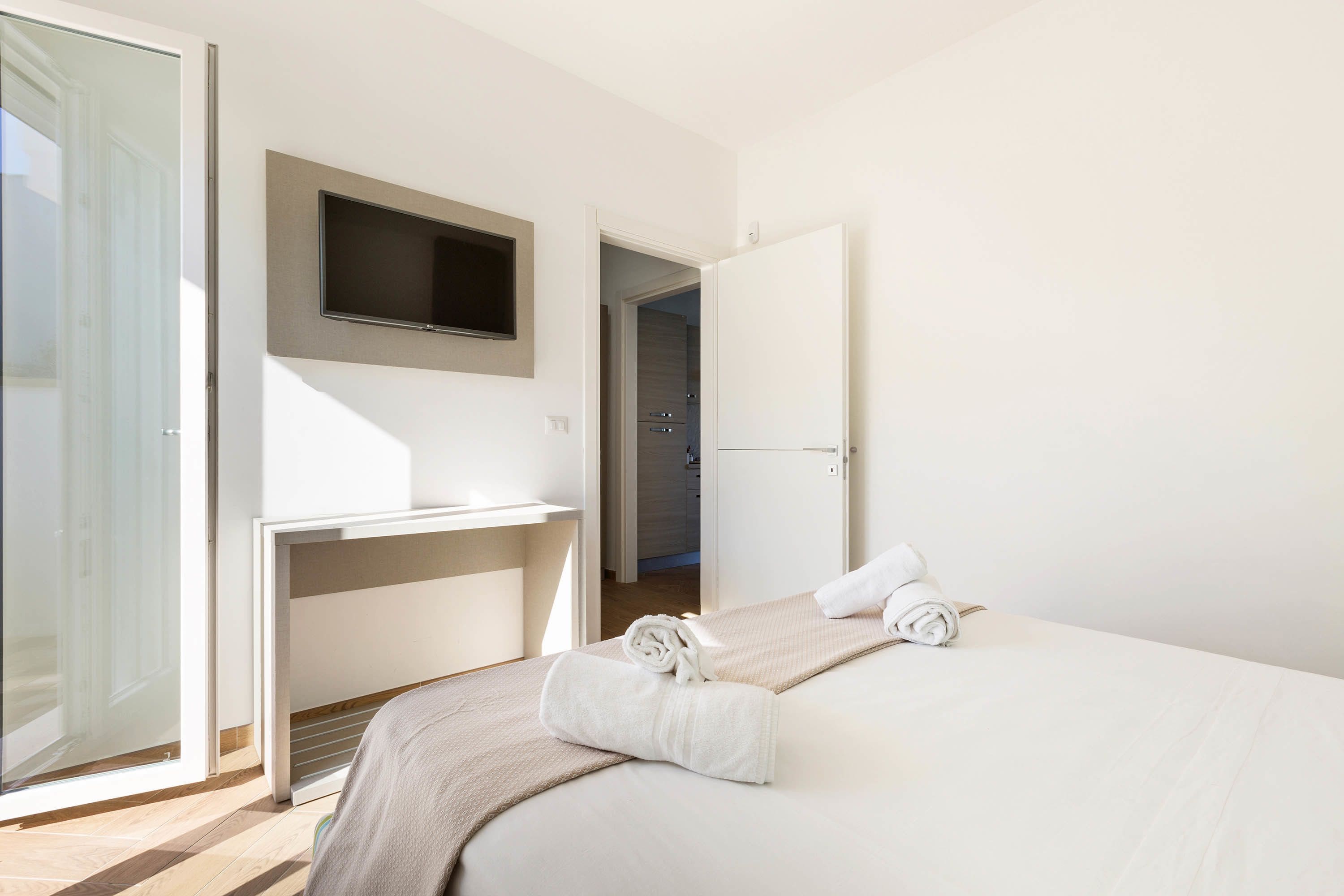 Habitación de hotel con cama, televisión montada en la pared, escritorio y puerta que da a un baño.