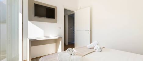 Habitación de hotel con cama, televisión montada en la pared, escritorio y puerta que da a un baño.