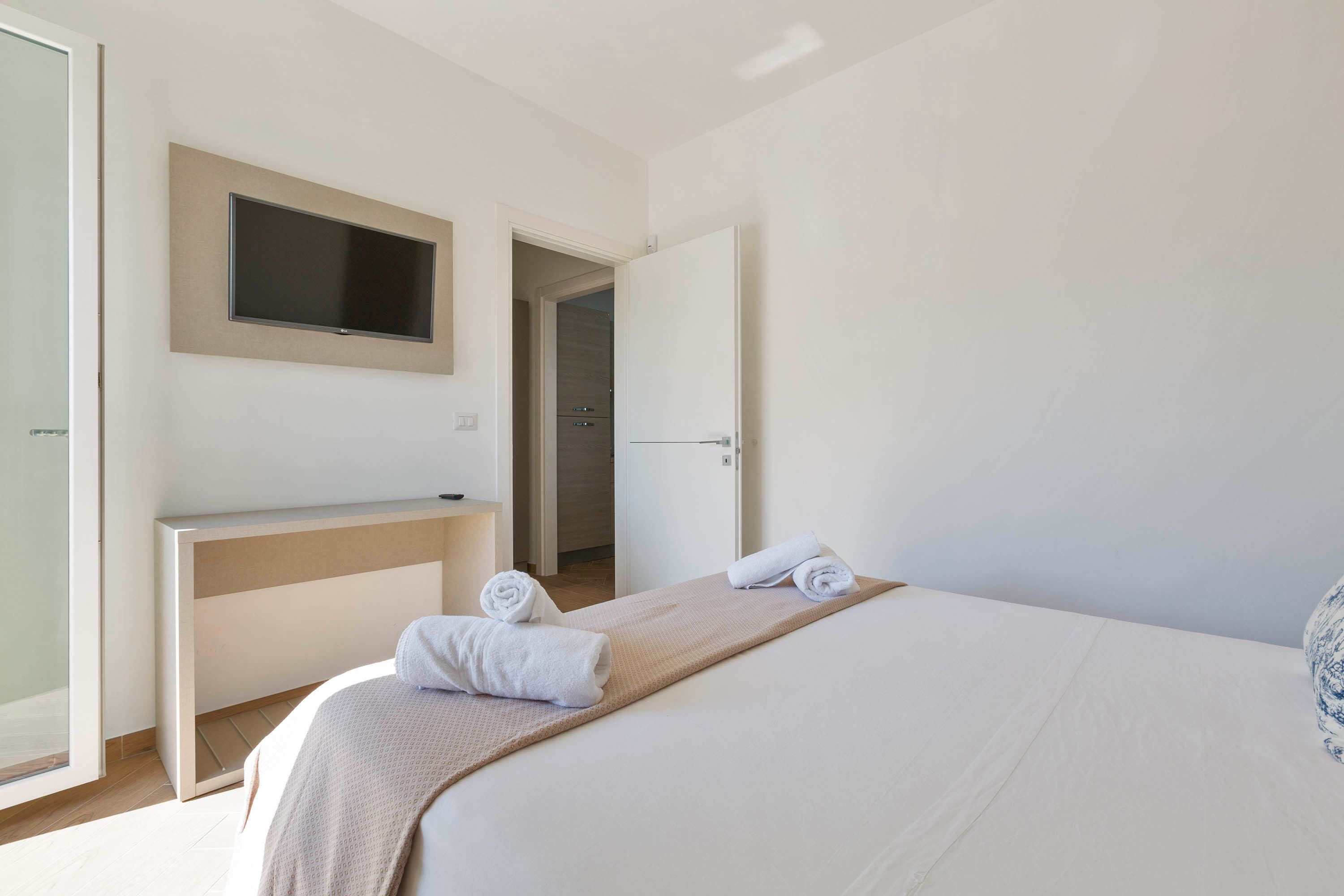 Ein Hotelzimmer mit einem Bett, einem an der Wand befestigten Fernseher, einem Schreibtisch und einem durch eine offene Tür einsehbaren Badezimmer.