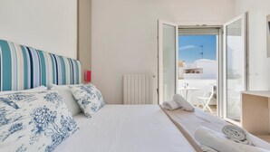 A hotel room with a bed, a view of the outside, and a balcony with chairs. - Absolute Suite Apartments (Porto Cesareo)