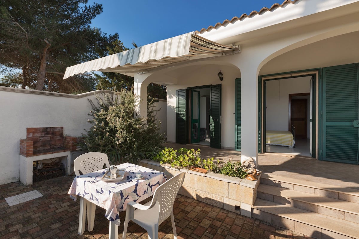 Un patio con mesa y sillas, una chimenea de ladrillo y una zona cubierta con toldo a rayas.