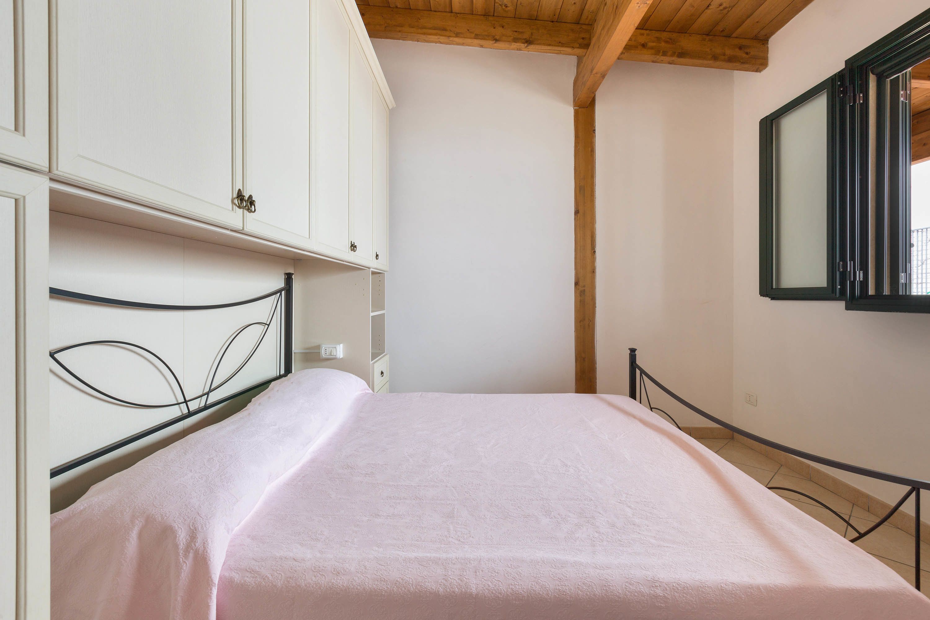 A bedroom with a bed, white wardrobe, and a window with a black frame.