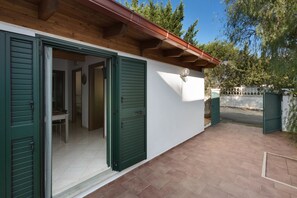 A house with green shutters, a tiled patio, and a visible interior with a dining area. -  Corallo Apartments by Barbarhouse (Porto Cesareo)