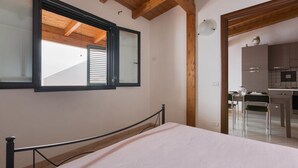 A bedroom with a bed, a window with blinds, and a view of a kitchen area. -  Corallo Apartments by Barbarhouse (Porto Cesareo)