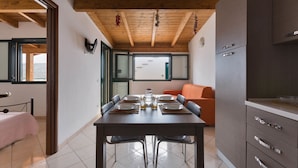 A dining area with a wooden ceiling, a table set for four, and a sofa in the background. -  Corallo Apartments by Barbarhouse (Porto Cesareo)