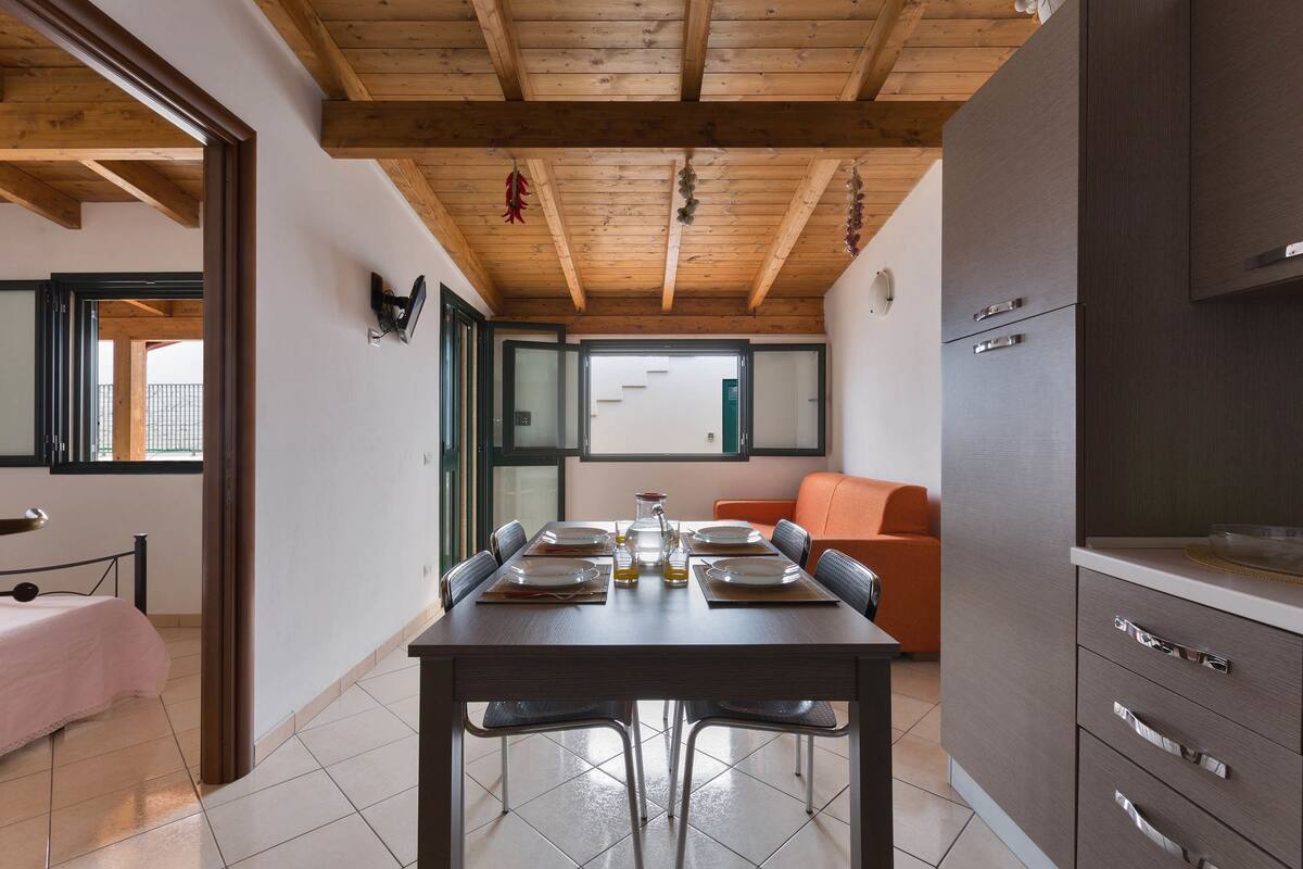 Un comedor con techo de madera, una mesa dispuesta para cuatro personas y un sofá al fondo.