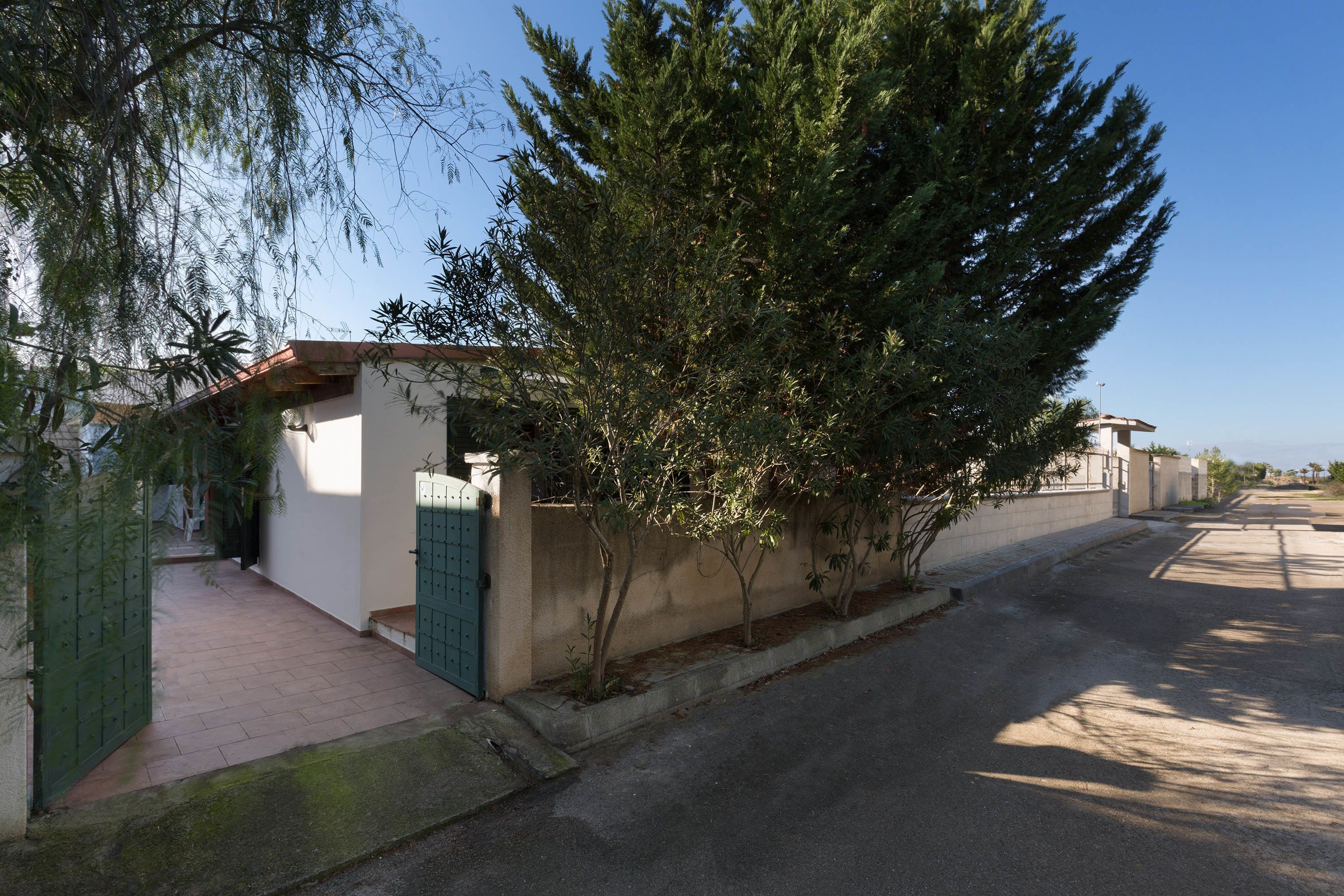 Une rue résidentielle tranquille, avec une petite maison, un portail vert et un arbre.