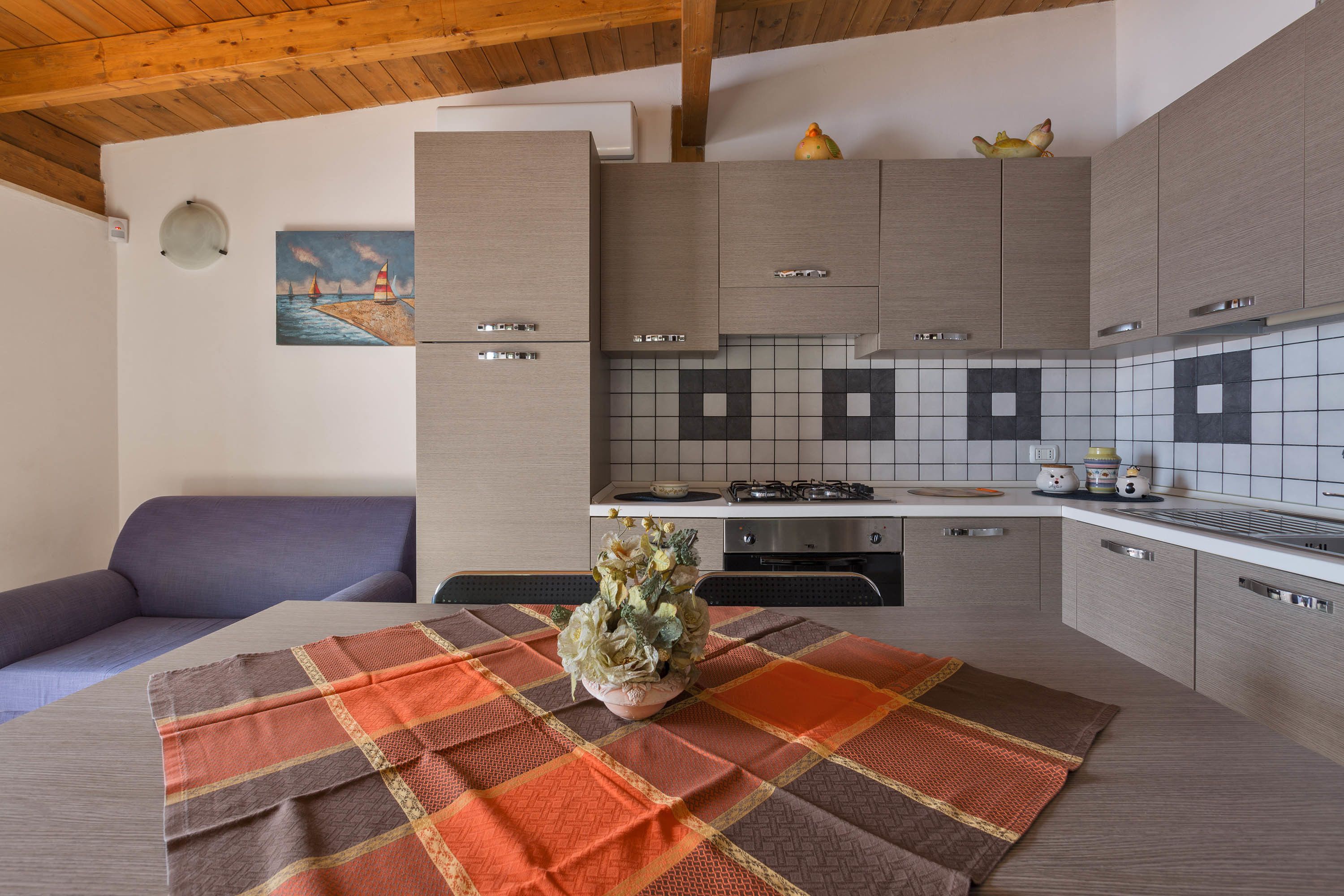 Cocina compacta con armarios grises, salpicadero de azulejos y comedor con mesa para dos.