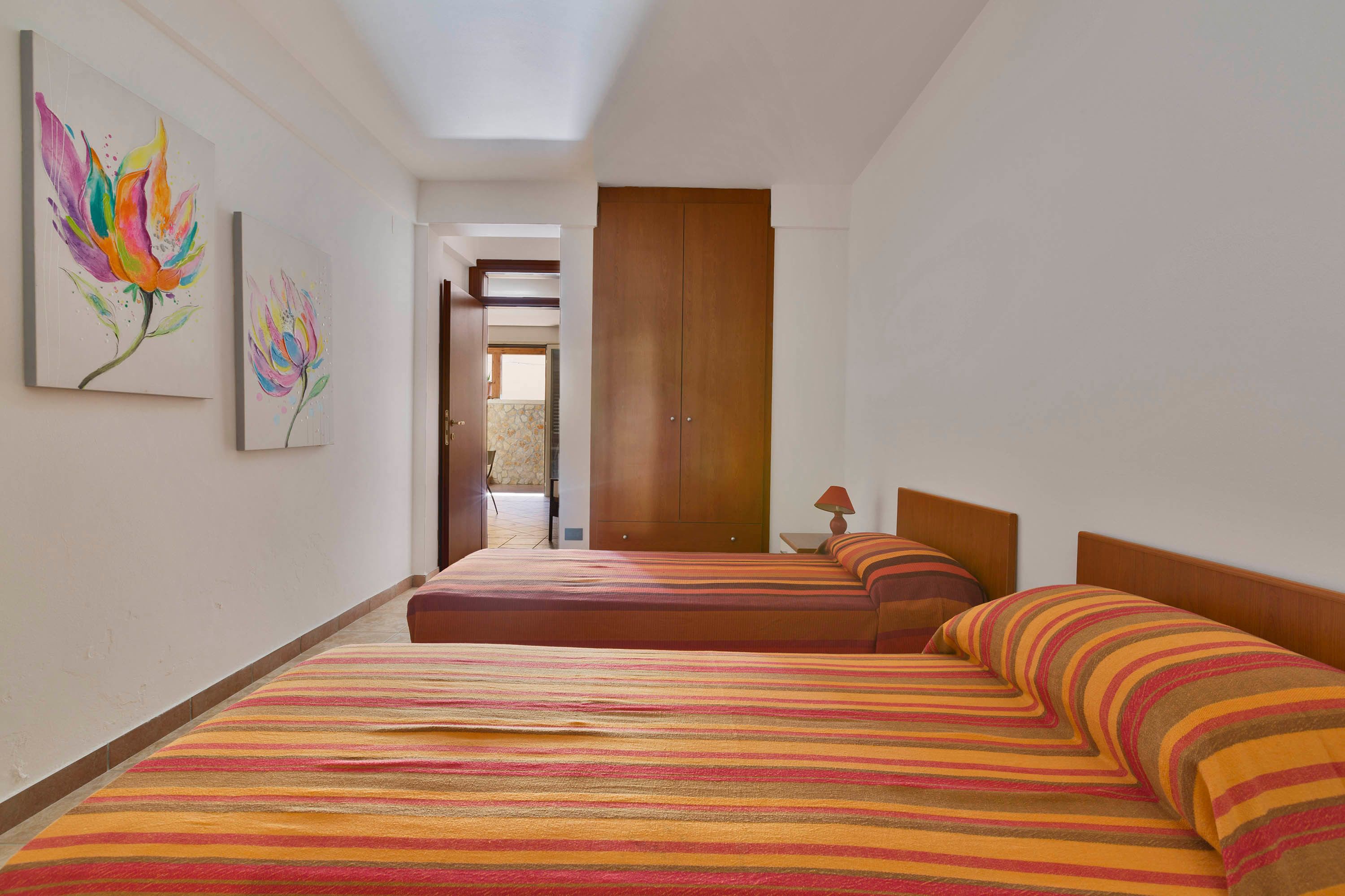 Habitación de hotel con dos camas, un armario de madera y dos cuadros en la pared.