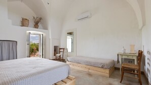 Un dormitorio con dos camas, un escritorio y una silla. Hay una ventana que proporciona luz natural y vistas al verdor exterior.