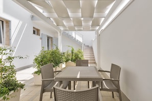 A covered outdoor patio with a table and chairs, potted plants, and a staircase leading to an upper level. - Residence Pianeta Mare (Porto Cesareo)