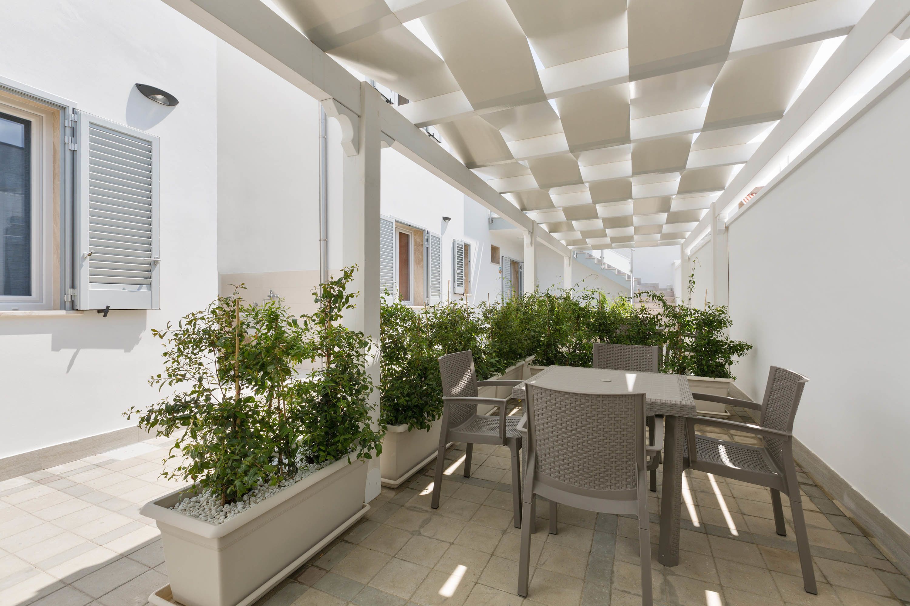 Ein Terrassenbereich im Freien mit Tisch, Stühlen, Topfpflanzen und einer Pergola.