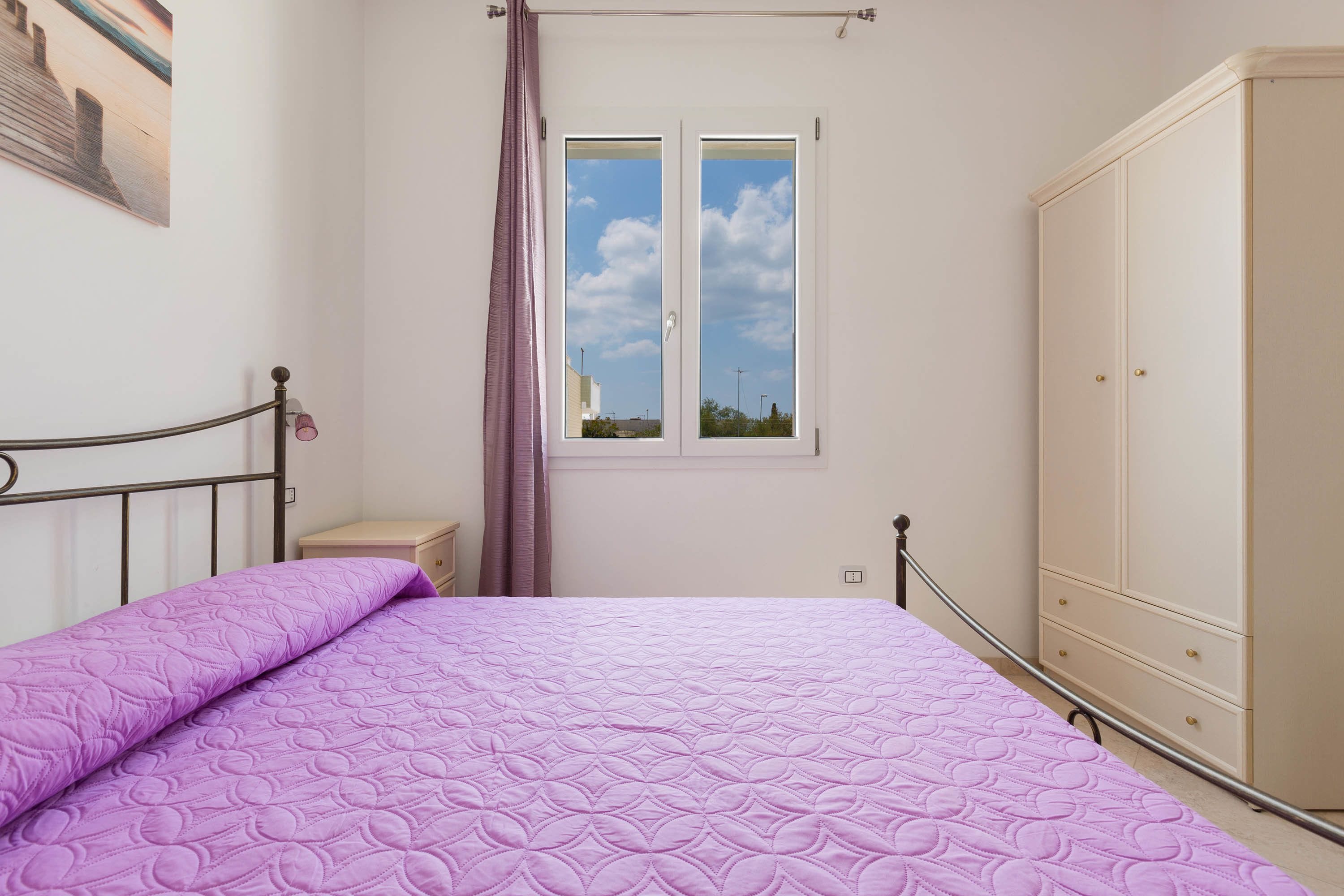 A bedroom with a bed, a wardrobe, a nightstand, a window with a view, and a curtain.