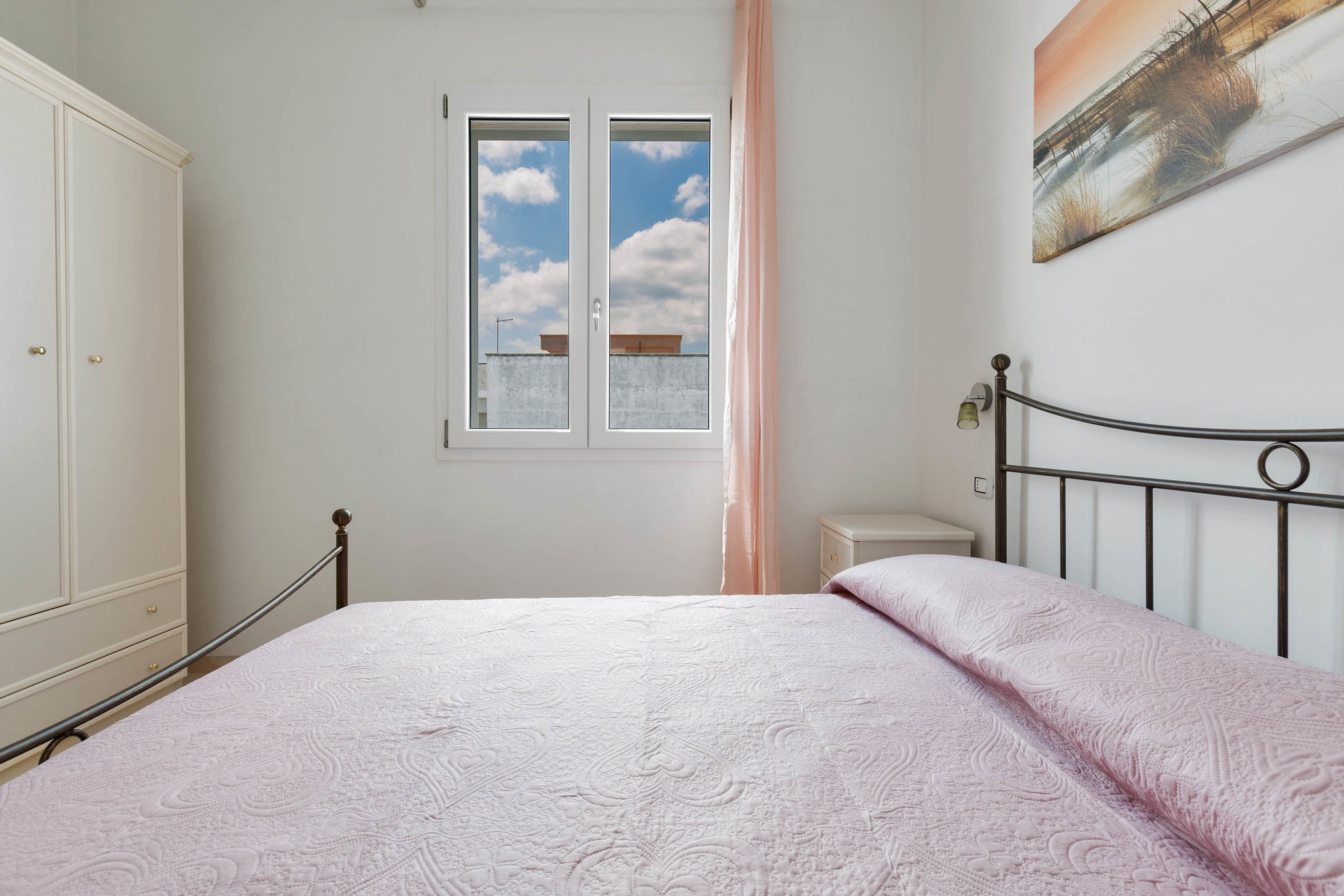 Een slaapkamer met een bed, een kledingkast, een raam met uitzicht op de lucht, en een schilderij aan de muur.