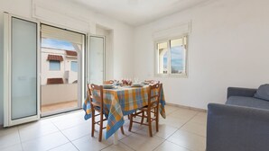 A dining area with a table set for four, a grey sofa, and a sliding glass door leading to a balcony. - Residence Tabù (Porto Cesareo)