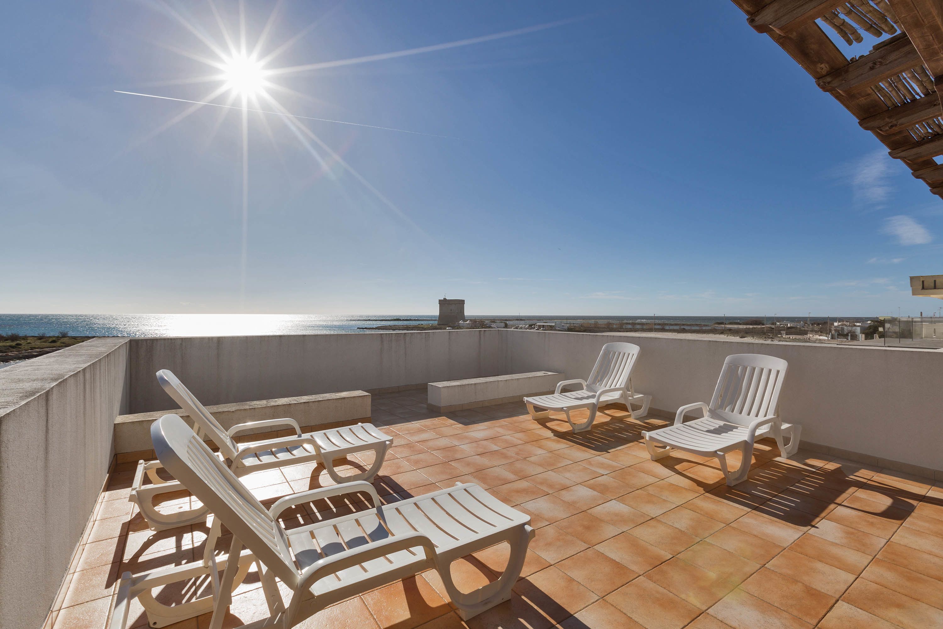 A rooftop terrace with white lounge chairs and a view of the sea.