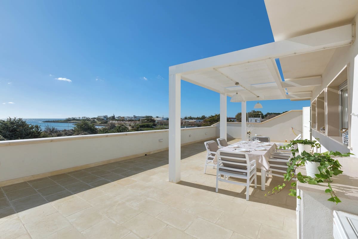 A rooftop terrace with a table and chairs, a potted plant, and a view of the sea.