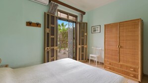 Een slaapkamer met een bed, een garderobe, een stoel en een raam met uitzicht op groen.